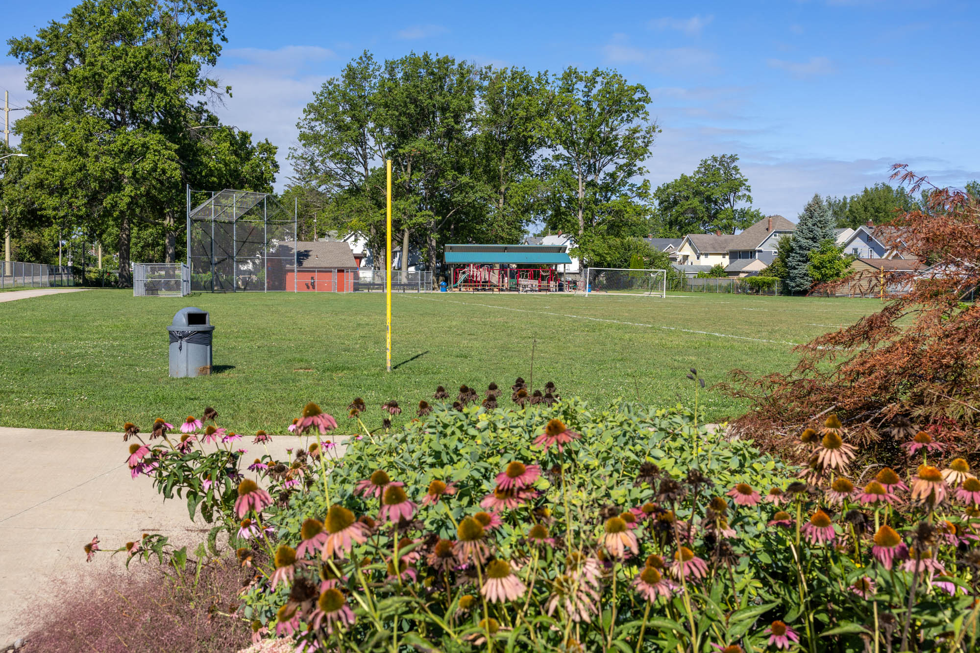 View of Cove Park from the parking lot. Grass baseball/soccer field and playground in the background.