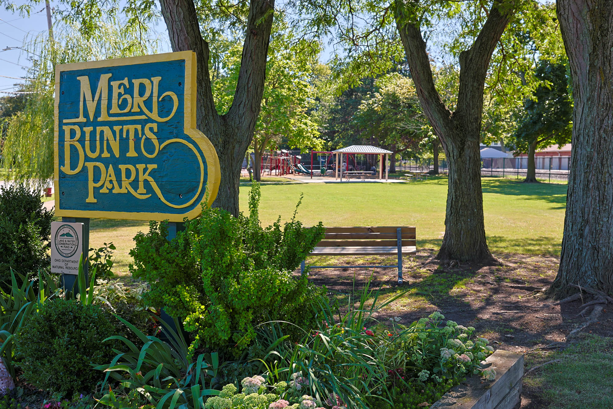Merl Bunts Park with wood sign in foreground, playground and pavilion in background.