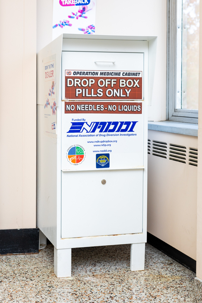 Photo of a white prescription medication drop box with a brown sign with white text that reads "Drop Off Box; Pills Only; No Needles, No Liquids".