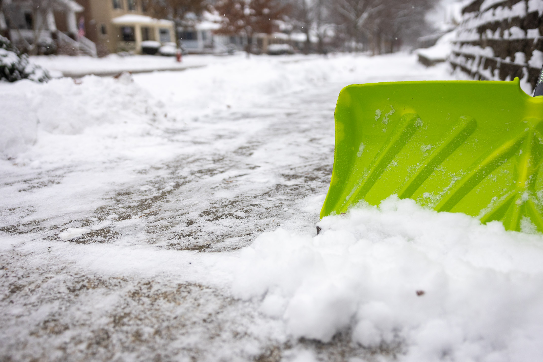 A green snow shovel on a Lakewood sidewalk with snow on the nearby surfaces.