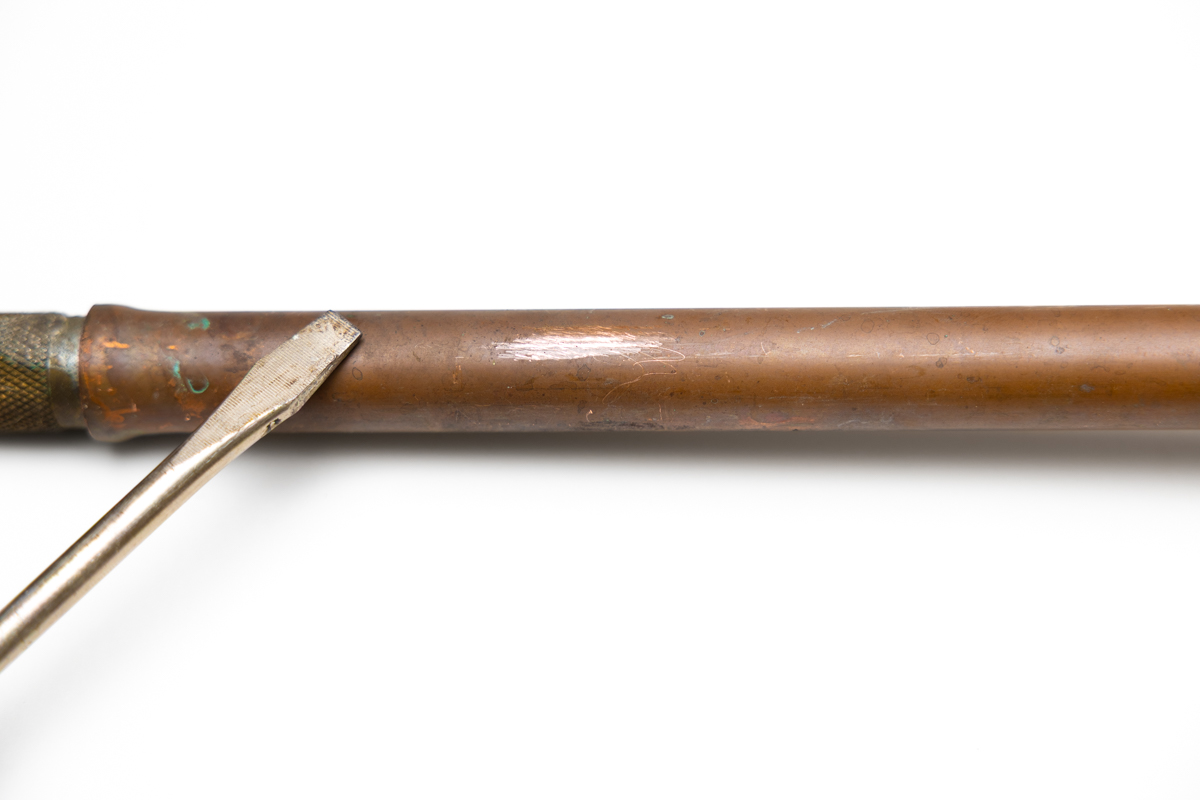 A copper pipe showing a shiny copper color when scratched by a screwdriver.