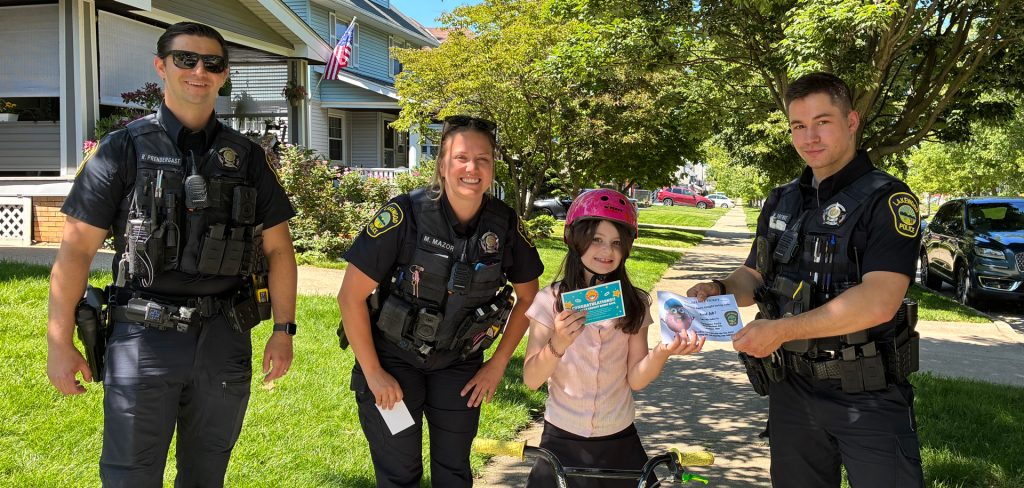 Three Lakewood Police officers pose with a young girl wearing a helmet on her bike. She is holding a certificate as part of the "Caught Being Safe" program.